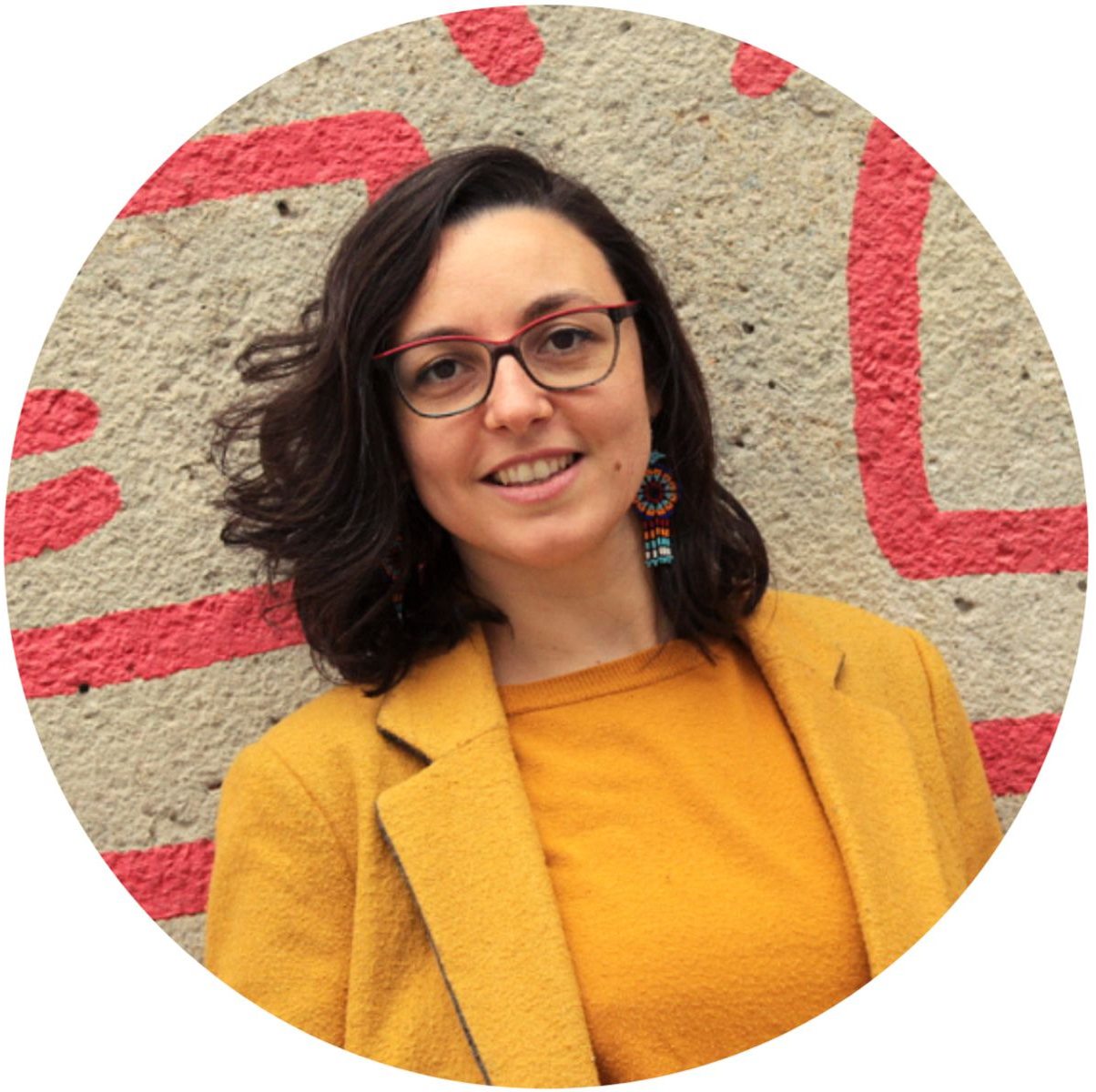 Alice Orrù è una donna con i capelli castani lunghi fino alle spalle e occhiali dalla grande montatura colorata.